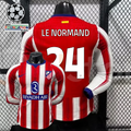  Front and back views of a red and white Atlético Madrid long-sleeve jersey with blue trim, white Le Normand number 24 print and Riyadh Air sponsor, alongside UCL graphics.