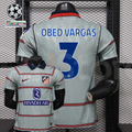 Front and back views of a light grey Atlético Madrid short-sleeve jersey with red horizontal stripes, blue Obed Vargas number 3 print and Riyadh Air sponsor, alongside UCL graphics.