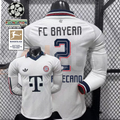 Front and back views of a white Bayern Munich long-sleeve jersey with a dark collar, red and dark detailing and Upamecano number 2 print, alongside UCL and Bundesliga patch graphics.