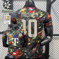 Front and back views of a black Bayern Munich short-sleeve jersey with a multicolored abstract design, cream Musiala number 10 print and Telekom sponsor, alongside UCL and Bundesliga graphics.