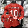 Front and back views of a red Bayern Munich long-sleeve home jersey with tonal stripes, white Musiala number 10 print and Telekom sponsor, alongside UCL and Bundesliga badge graphics.