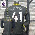 Chelsea dark grey long-sleeve jersey shown from the front and back, with white ESTÊVÃO 41 print, neon yellow details and a gold FIFA World Champions chest badge.
