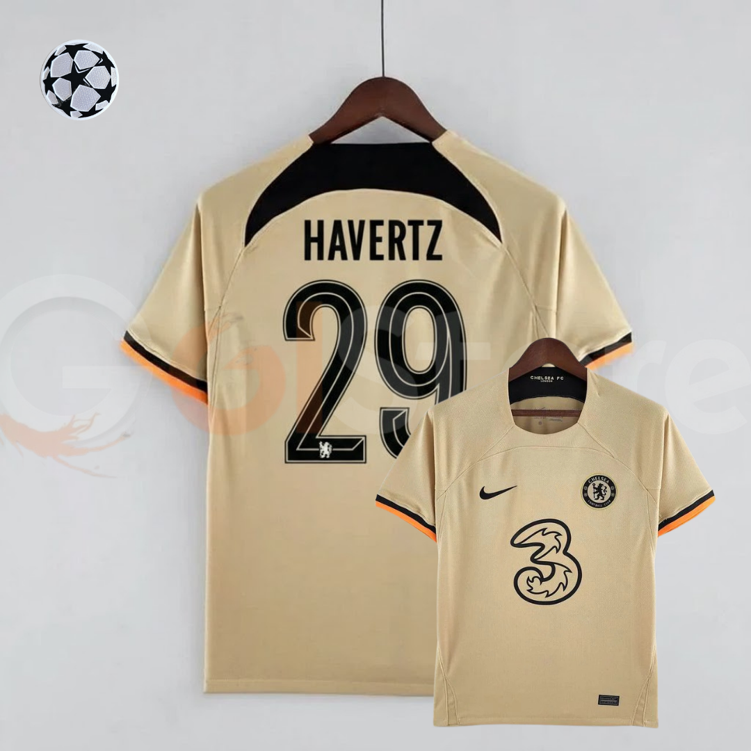 Front and back views of a pale gold Chelsea FC 2022–2023 short-sleeve third jersey with black Havertz #29 printing, a black upper back panel and black and orange sleeve trim.