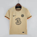 Front view of a pale gold Chelsea FC 2022–2023 short-sleeve third jersey with black chest logos and black and orange sleeve trim.