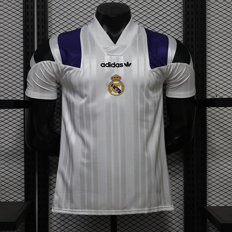 Front view of a white Real Madrid short-sleeve jersey with tonal vertical stripes, purple and black shoulder panels, a white collar, black adidas logo and centered club crest.
