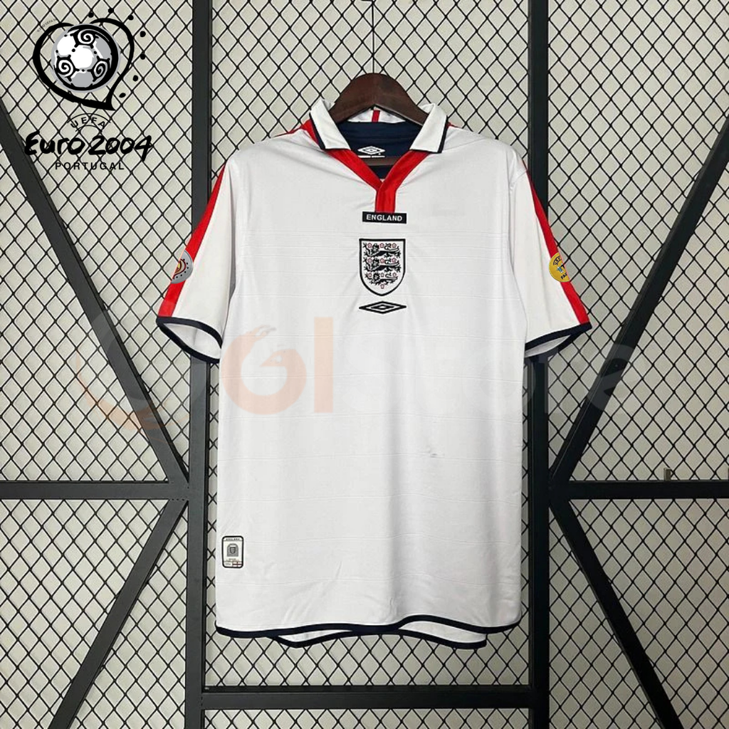 Front view of a white England short-sleeve retro home jersey with a polo collar, red shoulder panels, dark trim and a central Three Lions crest, alongside a EURO 2004 graphic.