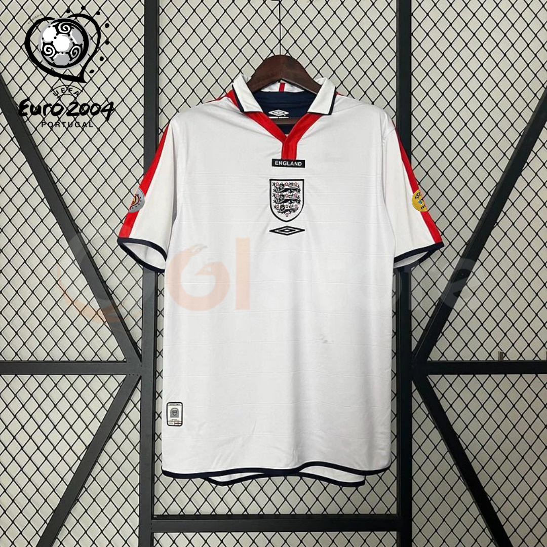  Front view of a white England short-sleeve retro home jersey with a polo collar, red shoulder panels, dark trim and a central Three Lions crest, alongside a EURO 2004 graphic.