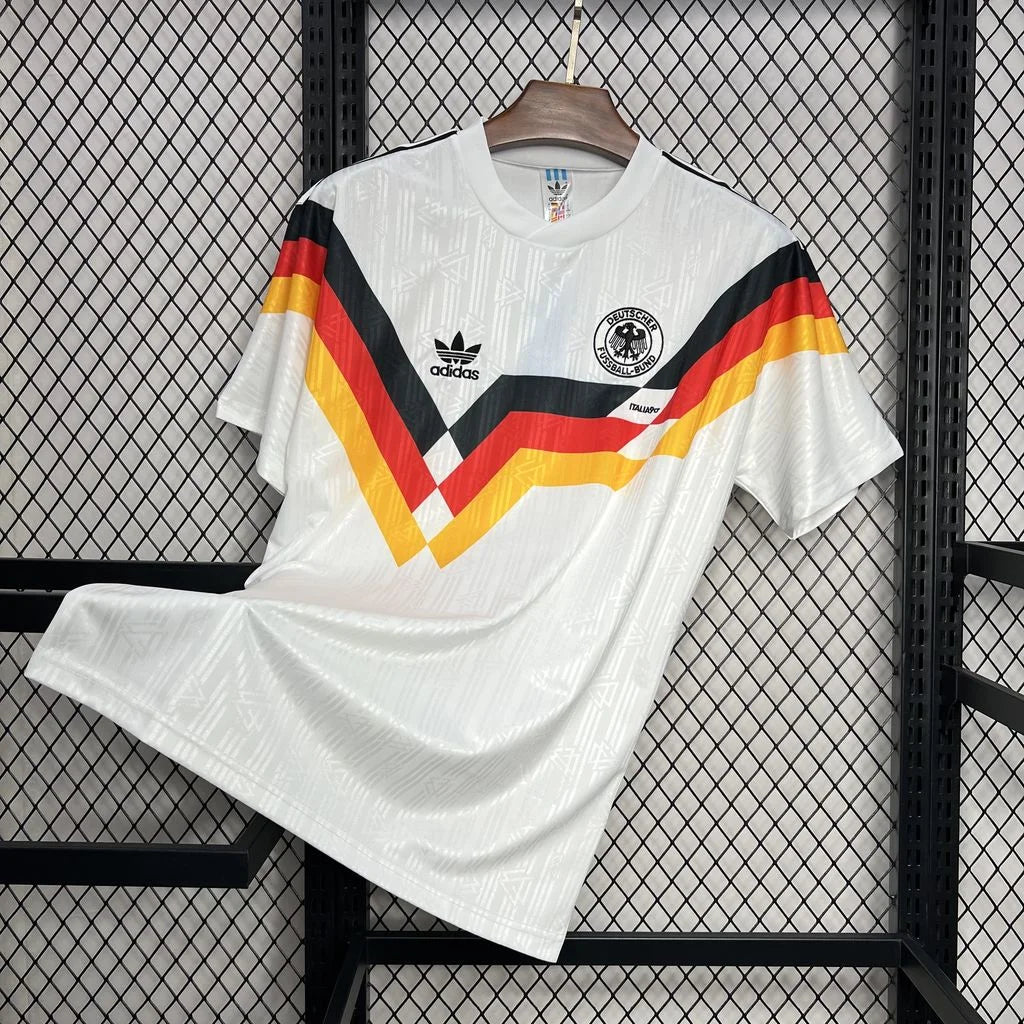 Front view of a white Germany 1990 retro short-sleeve home jersey with black, red and gold geometric chest stripes and the German football crest.