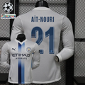 Front and back views of a white Manchester City long-sleeve jersey with blue central stripes, blue Aït-Nouri number 21 print and Etihad Airways sponsor, alongside UCL graphics.