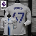 Front and back views of a white Manchester City long-sleeve jersey with blue central stripes and Foden number 47 print, alongside a Premier League graphic.