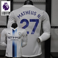 Front and back views of a white Manchester City long-sleeve jersey with blue central stripes and Matheus N. number 27 print, alongside a Premier League graphic.