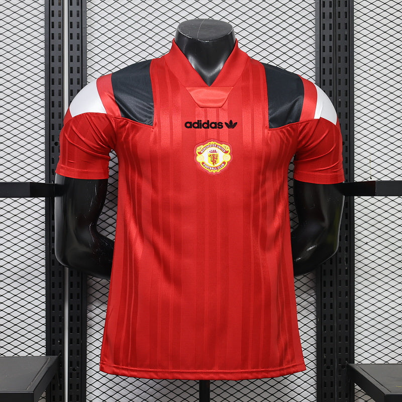 Front view of a red Manchester United short-sleeve jersey with tonal vertical stripes, black and white shoulder panels, a central club crest and black adidas logo.