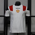 Front view of a white Manchester United short-sleeve jersey with red and black shoulder panels, a central club crest and black adidas trefoil logo.