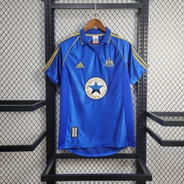 Front view of a blue Newcastle United retro short-sleeve away jersey with yellow shoulder stripes, a polo collar, club crest and circular Newcastle Brown Ale sponsor.